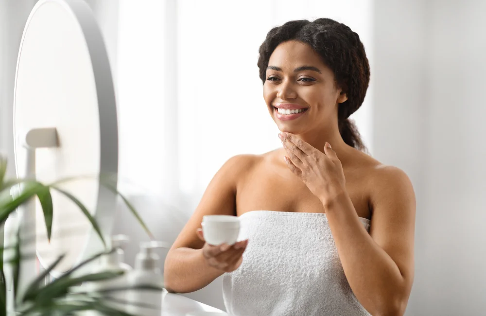 Smiling Black Woman Applying Moisturising Cream On Face